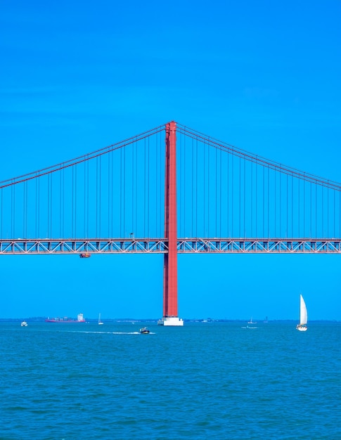 Barche a motore e a vela per container che navigano sul fiume Tago attraversando il ponte del 25 aprile