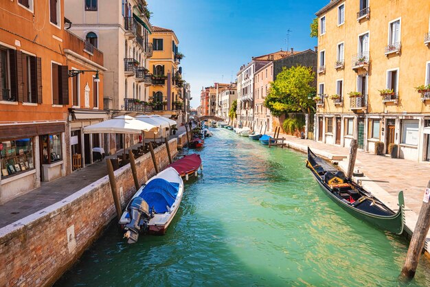 Barche a vela e gondola ormeggiate sul canale tra edifici residenziali con caffè sul marciapiede