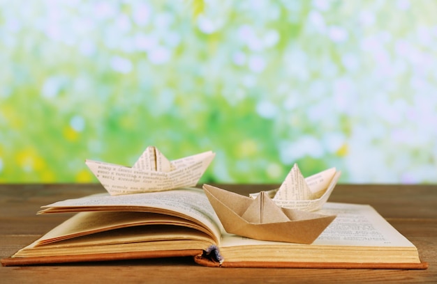 Barche di origami sul vecchio libro sulla tavola di legno all'aperto
