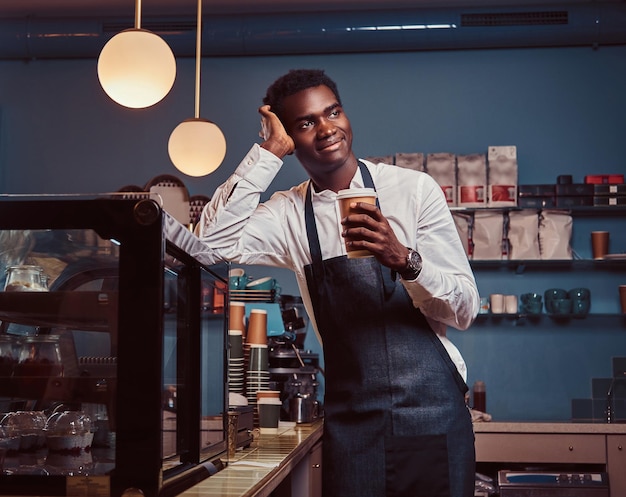 Barista africano che si rilassa dopo la giornata di lavoro con un caffè mentre si appoggia al bancone della caffetteria.