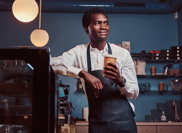 Barista africano che si rilassa dopo la giornata di lavoro con un caffè mentre si appoggia al bancone della caffetteria.