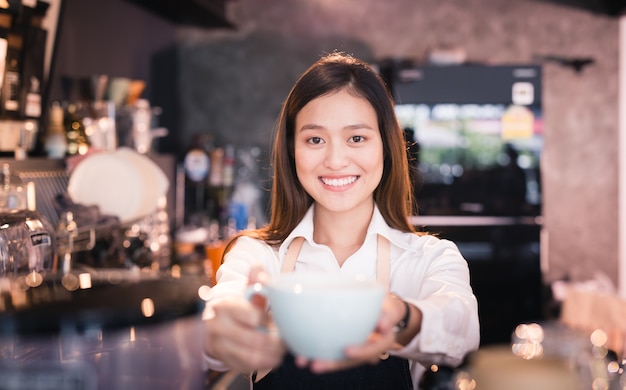 Barista asiatico della donna che sorride con una tazza di caffè in sua mano