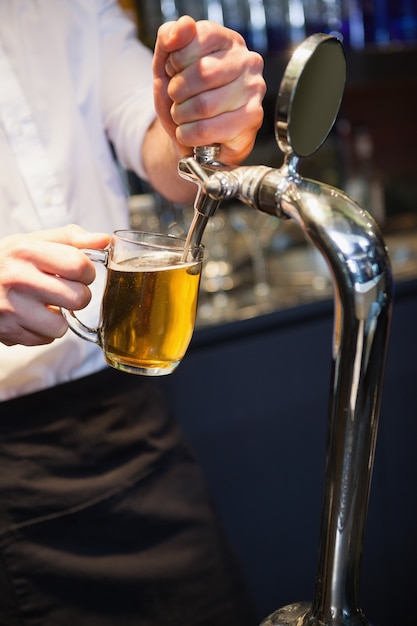 Barista bello che tira una pinta di birra