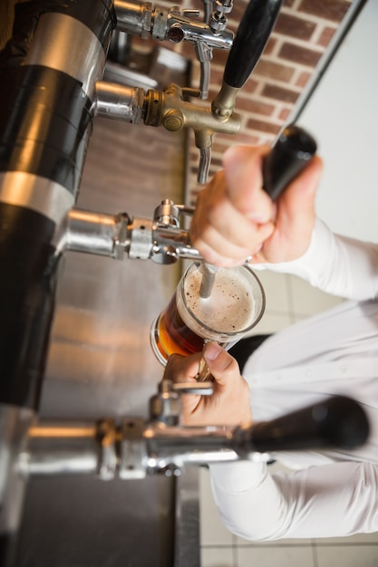 Barista bello che versa una pinta di birra