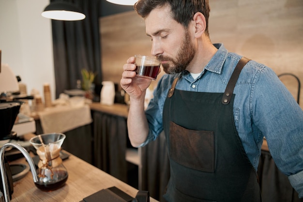 Barista bello con caffè filtro alla moda che odora di barba in caffetteria