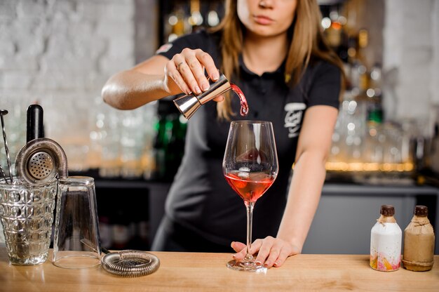 Barista bionda che fa cocktail al bancone del bar con attrezzatura da bar