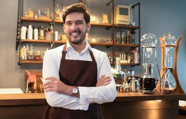 Barista caucasico bello del piccolo imprenditore della cameriera che sta in piedi in grembiule marrone che guarda la macchina fotografica