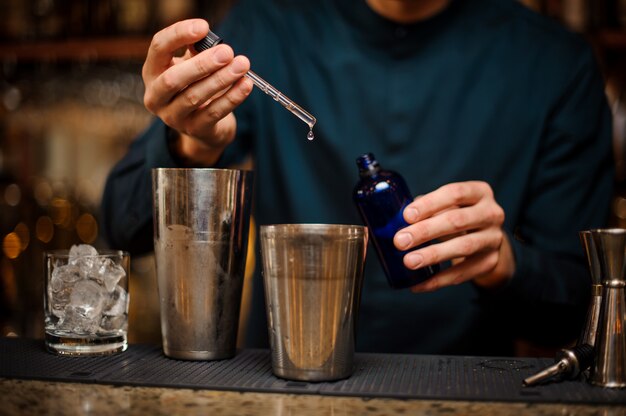 Barista che aggiunge un'essenza a uno shaker in acciaio con un cocktail alcolico