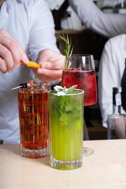 Barista che prepara cocktail alcolici con ghiaccio in bicchieri sul tavolo del bar