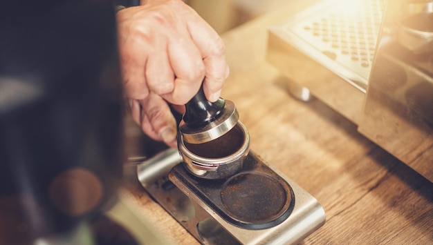 Barista che prepara il caffè, premendo la tempra sul portafiltro prima della preparazione, al bar