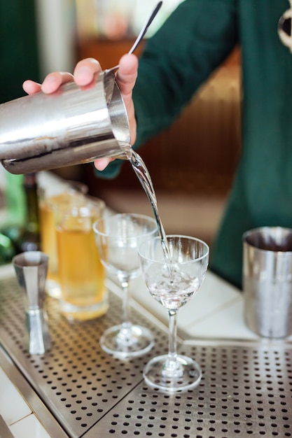 Barista che prepara un cocktail al bar: versando un drink da uno shaker in un bicchiere