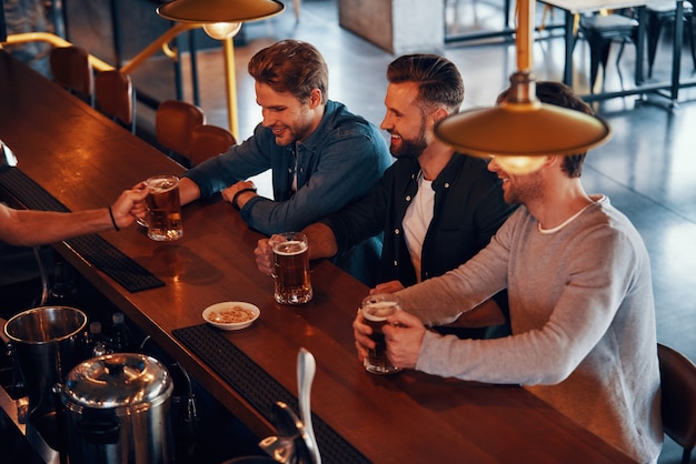 barista che serve birra ai giovani mentre si trova al bancone del bar in pub