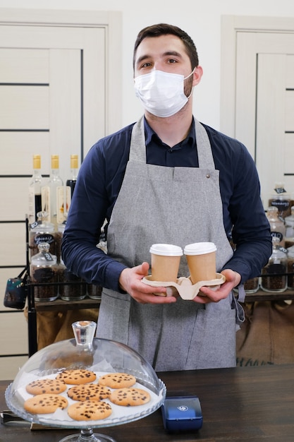 Barista che serve caffè in tazze da asporto in caffetteria in maschera