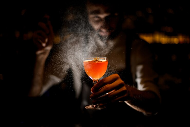 barista che serve un cocktail con una fetta di limone e un piccolo fiore giallo che spruzza su di esso nel buio