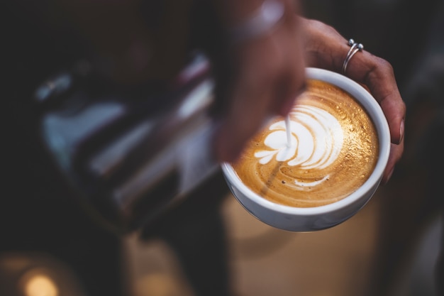 Barista che tiene e versa il latte per fare arte tarda.