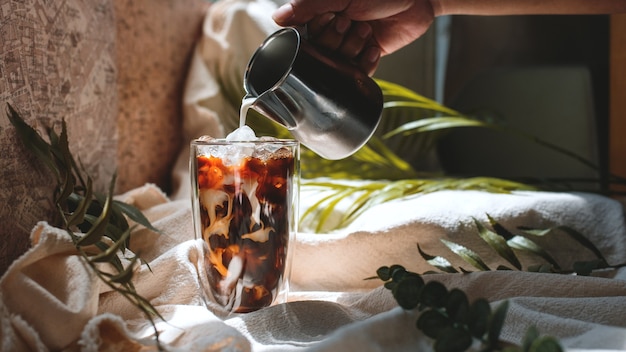 Barista che versa il latte in un bicchiere di caffè freddo