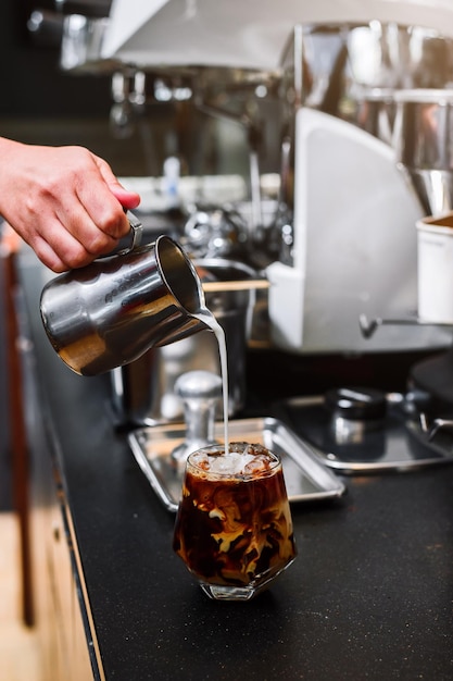 Barista che versa il latte in un bicchiere di caffè freddo