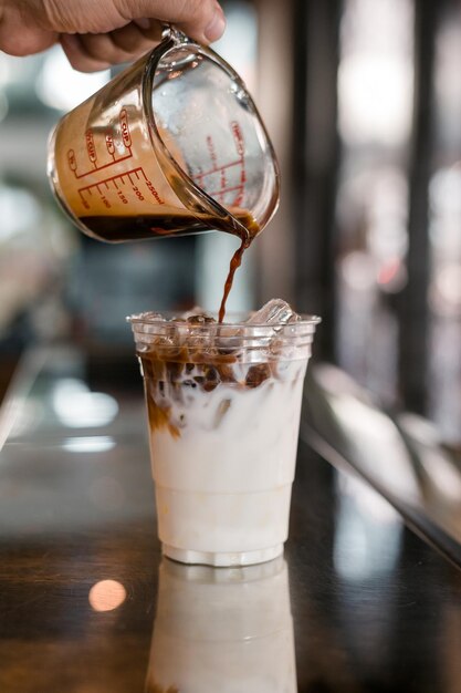 Barista che versa il latte in un bicchiere di caffè ghiacciato