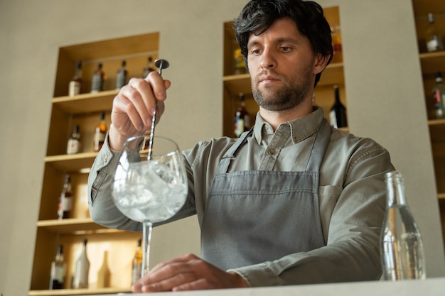 Barista con il grembiule che mescola un cubetto di ghiaccio nel bicchiere da cocktail