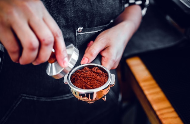 Barista con portafiltro e pressino per caffè che prepara un caffè espresso nella caffetteria