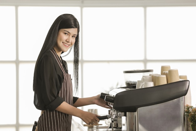 Barista donna che indossa un grembiule in piedi davanti alla macchina per il caffè e fa la bevanda nella caffetteria con fiducia in se stessi e modi amichevoli.