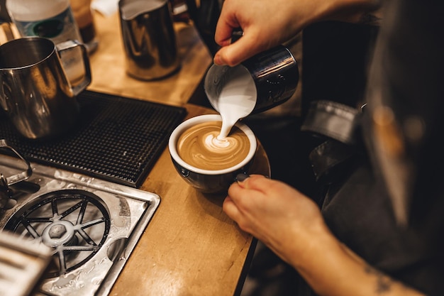 Barista donna che prepara latte art versando il latte schiumoso al vapore in un bicchierino di caffè espresso