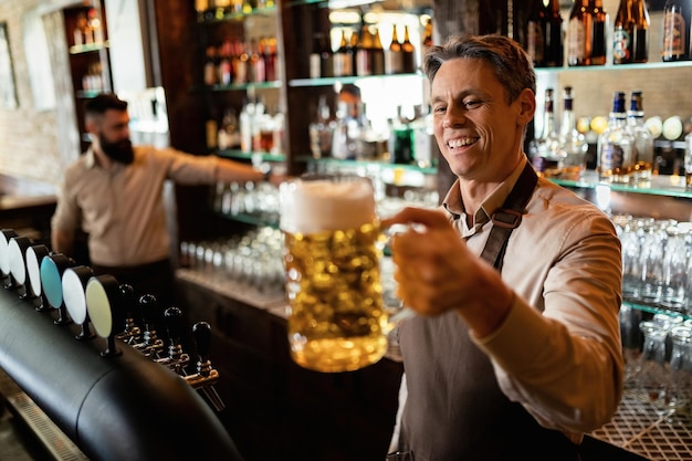 Barista felice che tiene un bicchiere di birra mentre lavora in un pub