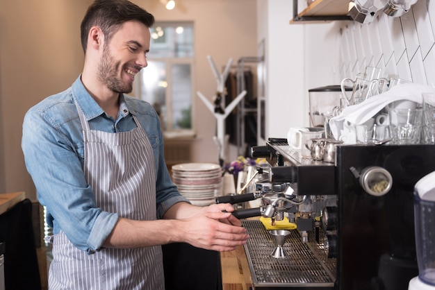 Barista felice. Giovane uomo bello che ride e che utilizza la macchina per il caffè in piedi dietro il bar