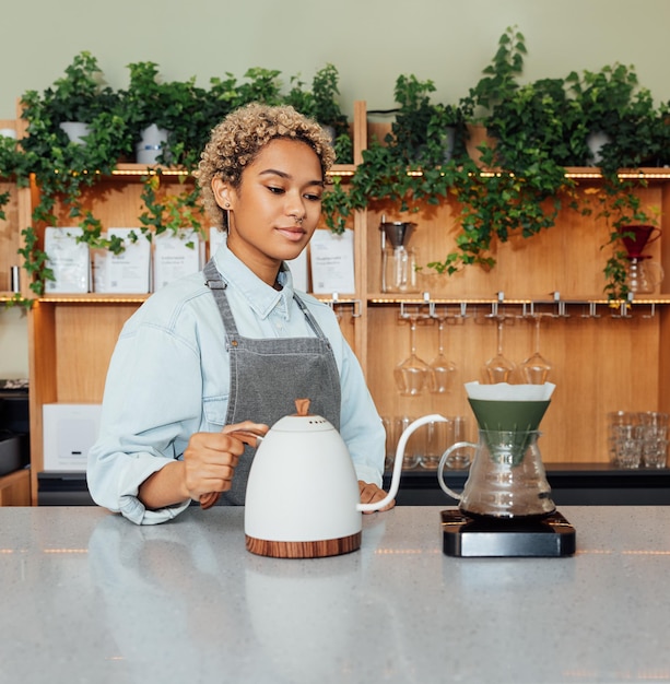 Barista femminile al bancone con un bollitore Giovane donna che fa il caffè con un filtro