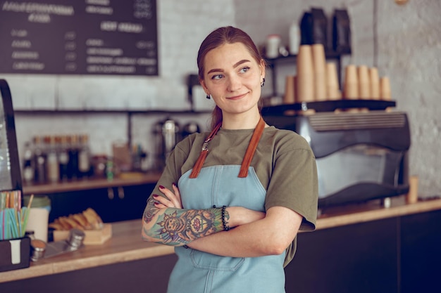 Barista femminile gioiosa in grembiule in piedi nella caffetteria