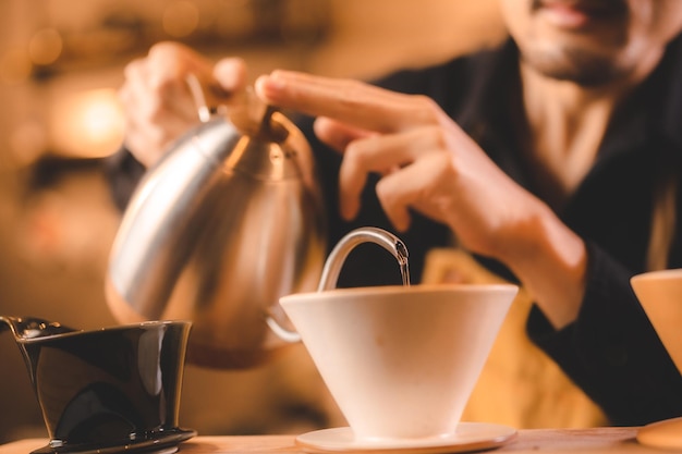 Barista hipster versando un'acqua calda per preparare il caffè con gocciolamento o filtro in stile caffè slow brew per bevanda aromatizzata alla caffeina bevanda in tazza caffè nero fresco ed espresso per colazione