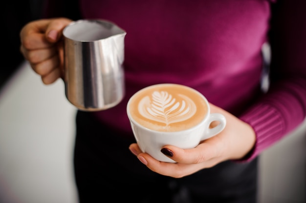 Barista in camicia viola che tiene una tazza di caffè con latte art