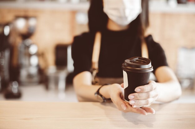 Barista in grembiule e maschera facciale in piedi dietro il bancone pronto a dare il servizio di caffè