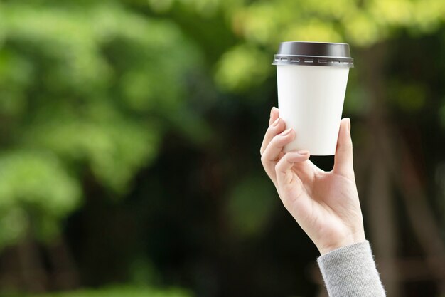 Barista in grembiule sta tenendo in mano il cappuccino caldo in un bicchiere di carta da asporto bianco.