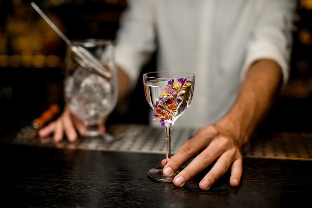 Barista maschio che serve un cocktail nel bicchiere decorato con fiori