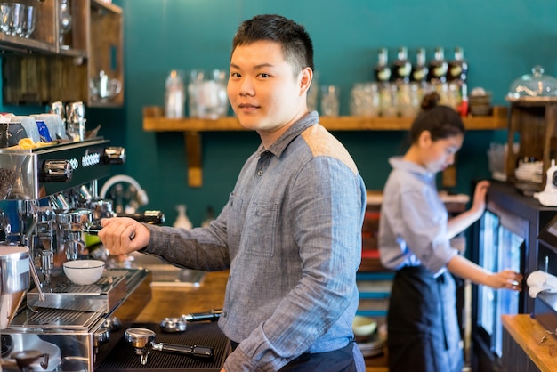 Barista maschio contento che utilizza la macchina del caffè espresso in caffè e che esamina macchina fotografica.