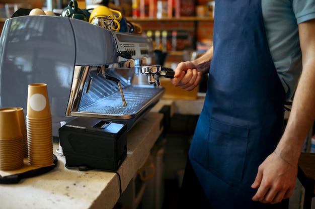 Barista maschio in grembiule prepara il caffè sulla macchina nella caffetteria