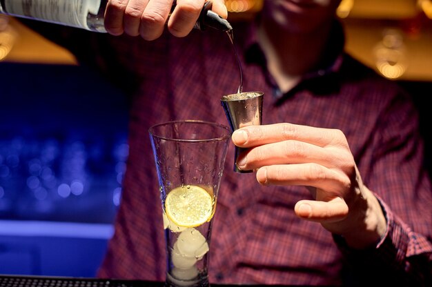 Barista maschio in una discoteca al lavoro che prepara un cocktail in un grande bicchiere.