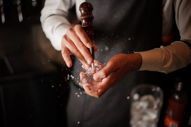 Barista maschio professionista che rompe un cubetto di ghiaccio per il cocktail