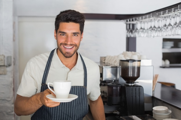 Barista maschio sorridente che tiene tazza di caffè al cafÃ ©