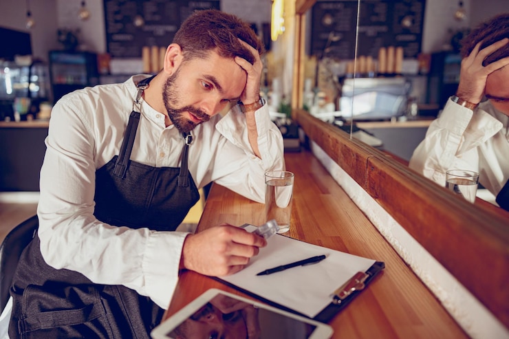 Barista maschio stanco con le pillole che si siedono al bancone di legno nella caffetteria