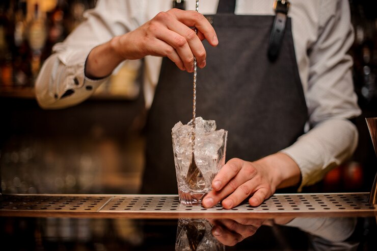 Barista mescolando ghiaccio nel bicchiere decorato sul bancone del bar