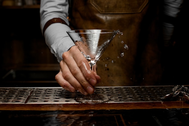 Barista professionista che mescola una bevanda alcolica nel bicchiere da martini con olive verdi