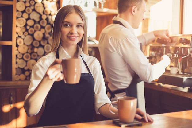 Barista professionista. Giovane donna e uomo in grembiule che lavorano al bancone del bar. Donna che tiene una tazza di caffè