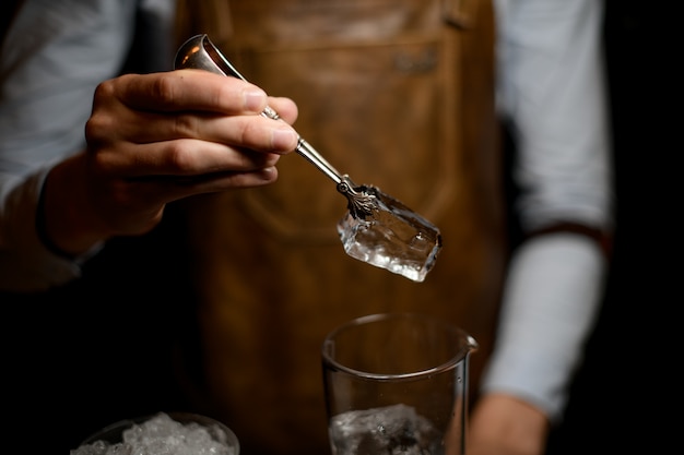 Barista professionista mettendo un grosso cubetto di ghiaccio nella tazza di vetro di misurazione