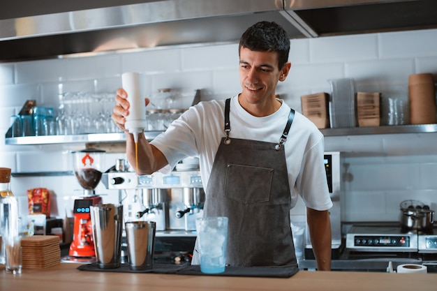 Barista professionista sorridente che prepara frappe ghiacciate al caramello mentre lavora nella caffetteria locale