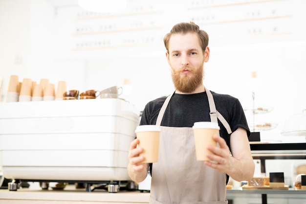 Barista sicuro che dà le tazze di caffè da portar via