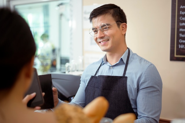 Barista sorridente che dà il pagamento online al cliente, paga l'ordine in un bar