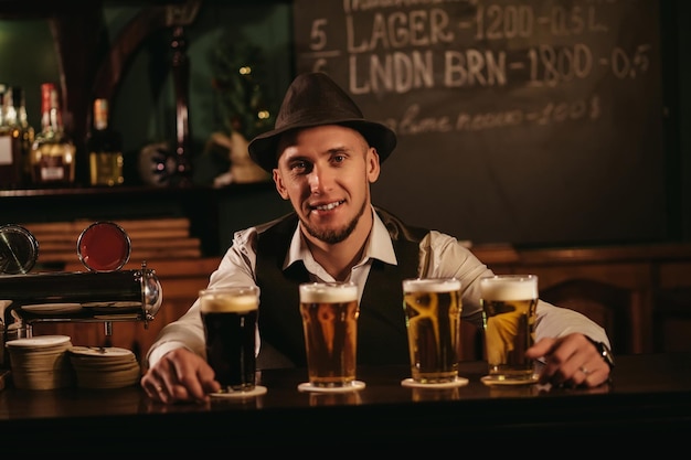 Barista sorridente felice al bancone del bar con quattro bicchieri di varie birre alla spina