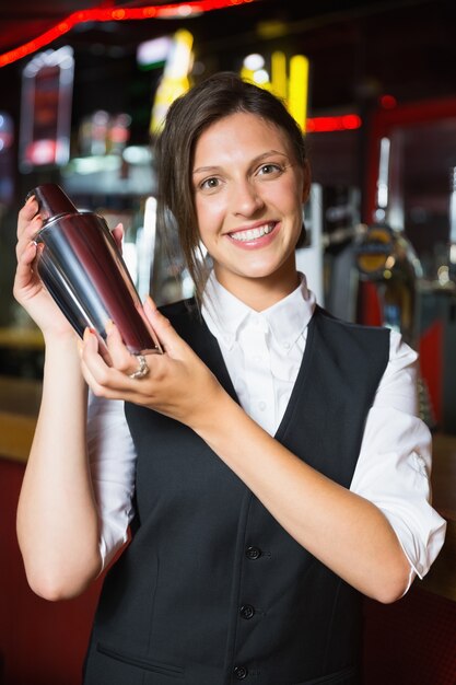 Barmaid felice che sorride alla macchina fotografica che fa cocktail